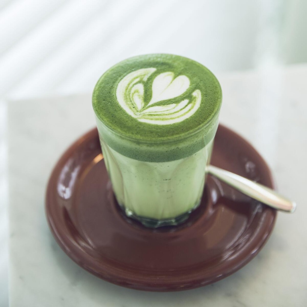 Matcha latte with heart latte art, served in a glass on a brown saucer