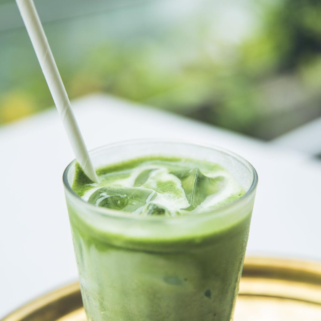 Iced matcha latte with a paper straw, on a gold tray